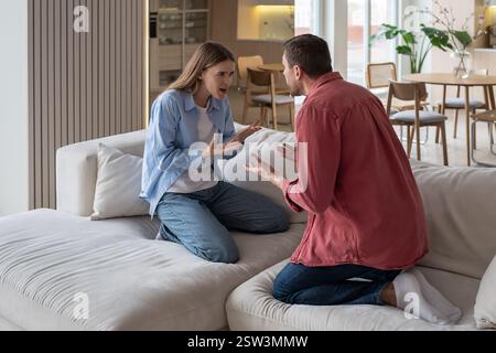 Couple en colère criant, se disputant sur le canapé. Homme, femme faisant des gestes agressifs, relation toxique Banque D'Images