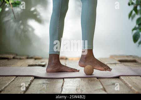 Femme noire se tient sur le tapis de gymnastique en utilisant la boule de massage pour rouler les pieds de tension passer du temps pour l'auto-soin. Banque D'Images