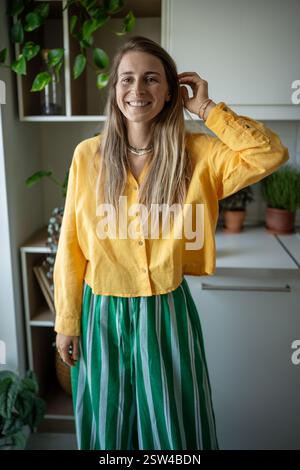Portrait femme joyeusement heureuse dans des vêtements jaunes regardant la caméra avec un sourire joyeux, touchant les cheveux. Banque D'Images