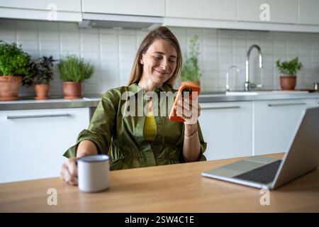 Souriante femme heureuse freelance travaillant procrastinant prendre pause, surfer sur le web dans le téléphone mobile. Banque D'Images