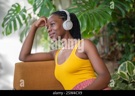 Rêve calme femme noire souriante dans des écouteurs écoutant de la musique détendue dans l'intérieur de la jungle urbaine. Banque D'Images