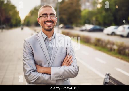 Portrait de jeune homme d'affaires heureux qui se tient dans la rue, regardant à distance et souriant. Banque D'Images