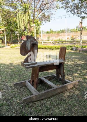 Un cheval à bascule en bois rustique se trouve dans le jardin paisible d'un petit café, entouré d'une végétation luxuriante et d'une atmosphère extérieure sereine, vue de face pour Banque D'Images