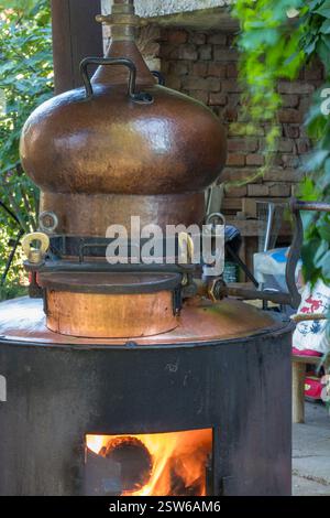 Une vue rapprochée d'un cuivre traditionnel encore utilisé pour la distillation, affiché à l'extérieur en plein soleil avec de la verdure en arrière-plan. Banque D'Images