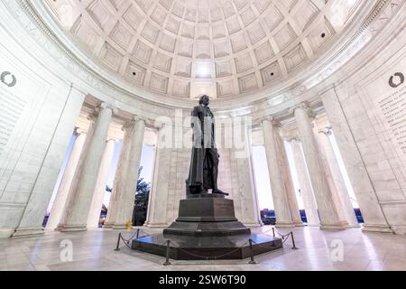 Mémorial Jefferson à Washington DC | WASHINGTON D.C., États-Unis — Le lever du soleil brille à travers la colonnade du Mémorial Jefferson, faisant ressortir en silhouette les colonnes ioniques autour de la statue en bronze de Thomas Jefferson par Rudulph Evans. Les panneaux muraux encadrant la figure portent des extraits de la Déclaration d'Indépendance et des écrits de Jefferson sur la liberté religieuse, encadrés de couronnes de laurier sculptées. La rotonde en marbre du mémorial, achevée sous la direction de l'architecte John Russell Pope, a été inaugurée en 1943. Banque D'Images
