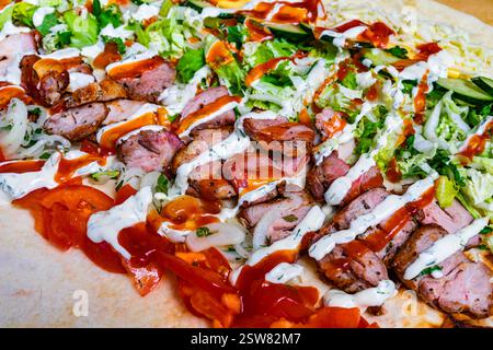 Les tranches de shish kebab sont artistiquement disposées sur une grande tortilla, recouvertes de laitue fraîche, tomates, oignons, et arrosées de sauces savoureuses, de mak Banque D'Images