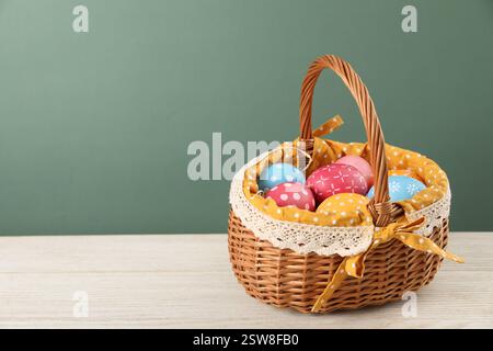 Beaucoup d'oeufs de Pâques décorés dans un panier en osier sur une table en bois sur fond vert, espace pour le texte Banque D'Images