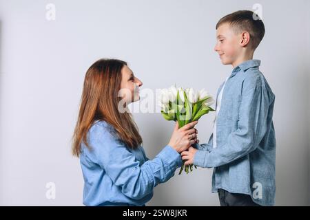 Le garçon donne des fleurs à sa mère et fait une surprise. Fête des mères, félicitations pour la journée internationale de la femme, fleurs en main. Banque D'Images