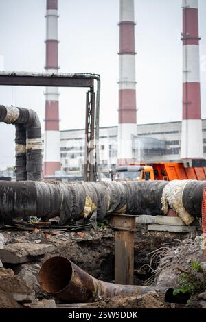 Tranchée creusée sur le chantier de construction avec cheminées derrière. Remplacement de tuyau pour chauffage, gaz, eau Banque D'Images