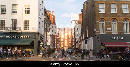 Les piétons traversent Baker Street, Londres, près des cafés Starbucks et Costa. La lumière du soleil met en valeur les bâtiments en briques rouges. Banque D'Images