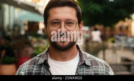 Portrait d'homme caucasien beau gars dans des lunettes homme voyageur touristique client unique des années 30 homme d'affaires à l'extérieur sourire calme regardant la caméra dans la ville Banque D'Images