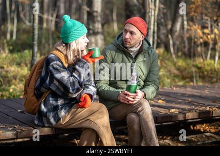 Homme détendu, femme se relaxant dans la forêt d'automne, boire du thé, communiquer, passer un bon moment tranquille ensemble Banque D'Images