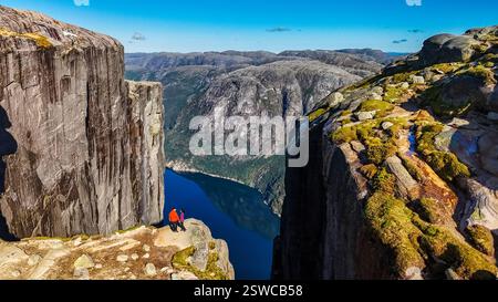 Deux individus se tiennent au bord du Kjeragbolten, falaise de Norvège, donnant sur une vue imprenable sur le fjord Banque D'Images