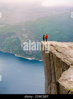 Deux individus se tiennent au bord de Preikestolen, une falaise spectaculaire en Norvège, contemplant la vaste étendue du fjord en contrebas Banque D'Images