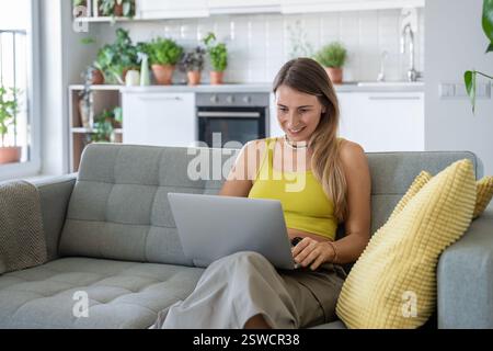 Femme souriante assis sur le canapé à la maison avec ordinateur portable souriant regardant l'écran recevoir de bonnes nouvelles dans le message. Banque D'Images