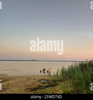 Un coucher de soleil serein au bord du lac avec des roseaux gracieux et des eaux calmes et paisibles reflétant le ciel Banque D'Images