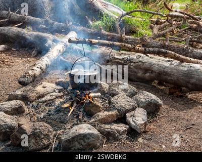 Cuisine de camping. Cuisson de nourriture au feu dans la nature. Bouilloire dans la suie suspendue au-dessus du feu. Survie dans la nature sauvage. Flamme merveilleuse avec c Banque D'Images