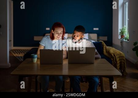 Jeune couple divers exécutant de petites entreprises en ligne à la maison, homme et femme travaillant sur des ordinateurs portables Banque D'Images