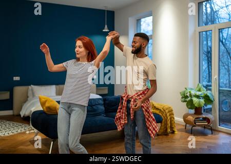 Joyeux couple multiracial romantique en amour apprenant à danser ensemble à la maison Banque D'Images