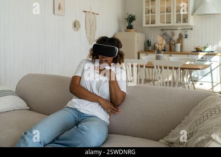 S'est demandé femme afro-américaine excitée lunettes virtuelles regarder un film, jouer à des jeux vidéo. Banque D'Images