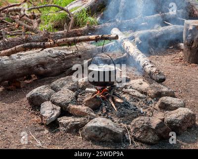 Cuisine de camping. Cuisson d'aliments. Bouilloire dans la suie suspendue au-dessus du feu. Banque D'Images