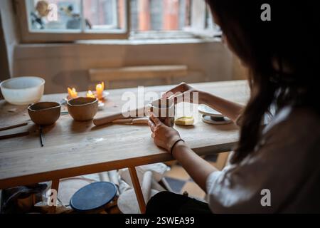 Les mains des femmes mouillent et alignent le gobelet en argile avec l'éponge sur la table du studio. Vaisselle artisanale, artisanale Banque D'Images