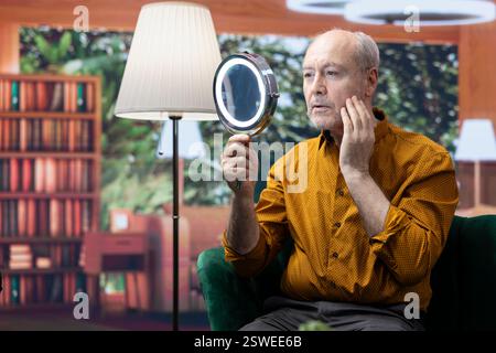 Homme âgé appliquant du sérum et de la crème hydratante sur ses joues, dorlotant la routine quotidienne de soins de la peau pour préserver la peau vieillissante. Personne utilisant la lotion rajeunissante pour le toilettage, soins personnels. Banque D'Images