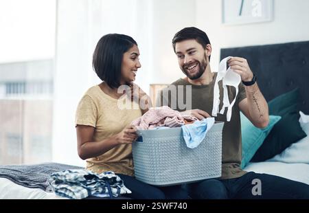Blanchisserie, plier les vêtements et couple dans la chambre à coucher pour le nettoyage, la routine de corvée et l'hygiène à la maison. Mariage, relation et heureux homme et femme avec Banque D'Images