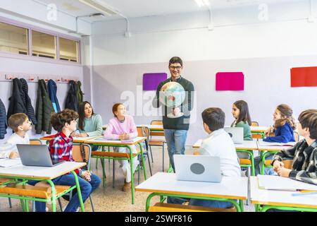 Professeur de géographie engager les élèves tout en tenant un globe, favoriser l'apprentissage et la compréhension dans un environnement de classe dynamique Banque D'Images