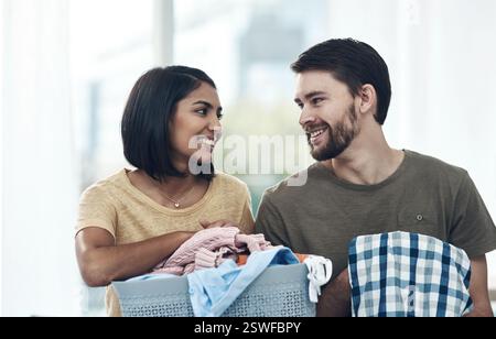 Lessive, heureux et couple plient les vêtements dans le panier pour le nettoyage, la routine de corvée et l'hygiène à la maison. Mariage, relation et homme et femme avec Banque D'Images
