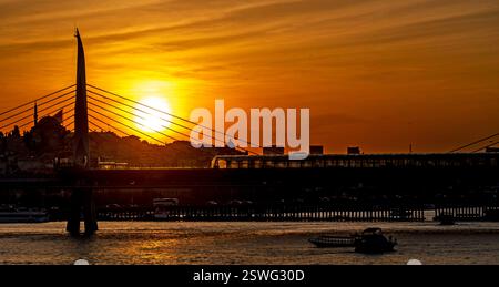 Un magnifique coucher de soleil sur un paysage urbain avec un pont et des bateaux sur l'eau. Le ciel est peint avec des teintes chaudes d'orange et de jaune, se reflétant sur th Banque D'Images