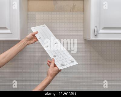 Gros plan du collage d'un panneau de planche blanche en plastique sur le mur. Main de l'homme tenant et utilisant le pistolet à colle Banque D'Images