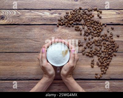 Tasse de cappuccino à la main. Grains de café sur la table. Banque D'Images