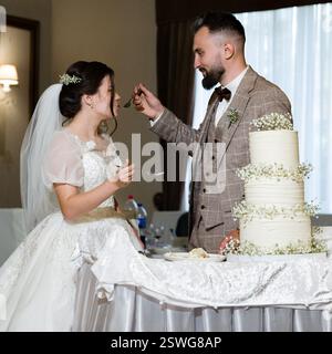 Le marié nourrit le gâteau de mariage de mariée, un doux moment de bonheur nouveau lywed. Banque D'Images