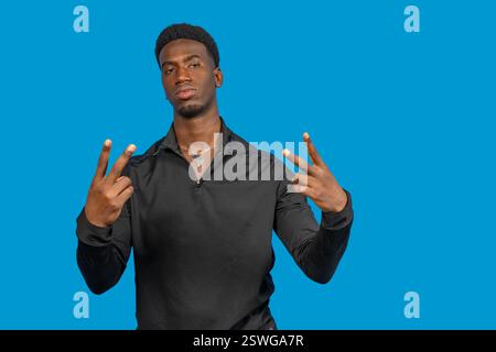 Jeune homme confiant geste signe de paix avec les deux mains sur un fond bleu vif Banque D'Images