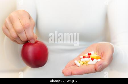 Une personne tient une pomme rouge dans une main et un mélange de compléments alimentaires colorés dans l'autre main, symbolisant les choix de santé. Banque D'Images