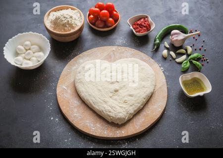 Pâte en forme de coeur et un ensemble d'ingrédients pour pizza sur une table noire. La vue depuis le haut Banque D'Images