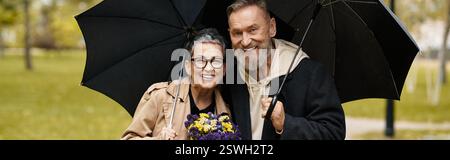 Couple aimant profite d'un moment joyeux ensemble à l'extérieur, tenant un parapluie et des fleurs à l'automne. Banque D'Images