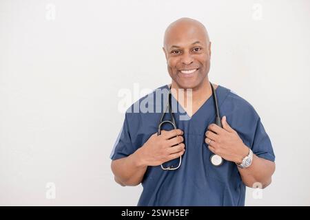 Professionnel de santé souriant dans des gommages bleus tenant un stéthoscope Banque D'Images