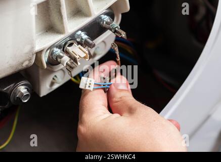 La main du maître retire les puces électriques pour retirer l'élément chauffant de la machine à laver et le capteur de chauffage. Réparation du lavage mac Banque D'Images