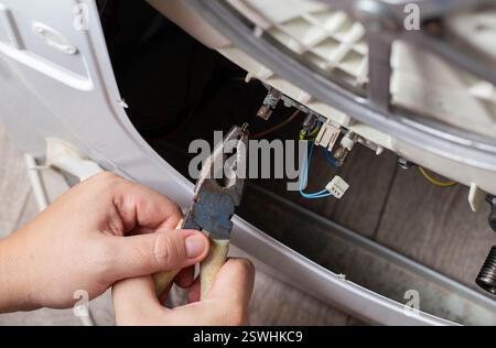 La main du maître retire les puces électriques pour retirer l'élément chauffant de la machine à laver et le capteur de chauffage. Réparation du lavage mac Banque D'Images