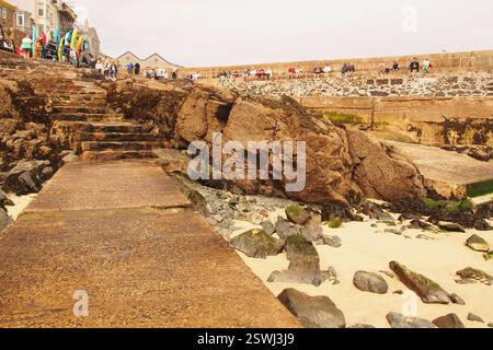 Vacanciers debout et assis sur New Pier St Ives, Cornouailles, Angleterre Royaume-Uni, regardant vers la mer et les bains de soleil avec planches de surf en vente Banque D'Images