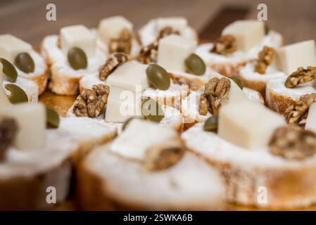 Tranches de baguette garnies de noix à la crème au fromage et d'olives vertes disposées sur une surface en bois Banque D'Images