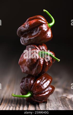 Trois poivrons habanero au chocolat mûrs (capsicum chinense) sur une table en bois. Poivrons mexicains très chauds sur la table en bois rustique de près Banque D'Images