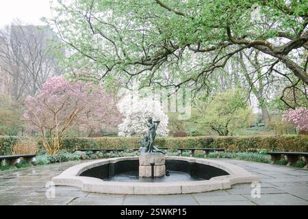 Les couleurs printanières éclatent dans un jardin serein doté d'une fontaine en pierre entourée d'arbres fleuris vibrants. Banque D'Images