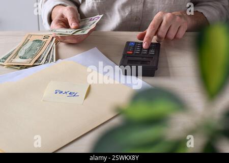 Femme assise à un bureau comptant des dollars américains en argent comptant avec une calculatrice faisant des impôts Banque D'Images