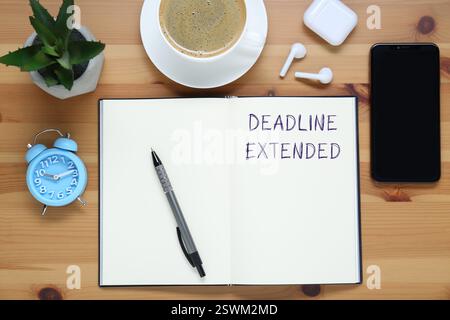 Texte Deadline Extended in Notebook, stylo, réveil, téléphone portable, écouteurs et café sur table en bois, plat Banque D'Images