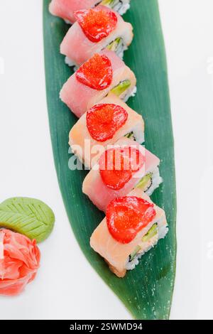 Rouleaux de sushi frais agencés habilement sur une feuille avec des garnitures vibrantes et des éléments décoratifs Banque D'Images