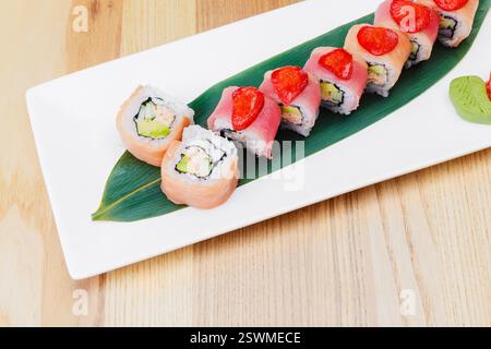 Plateau de sushi coloré avec divers rouleaux et garnitures fraîches servies sur une feuille Banque D'Images