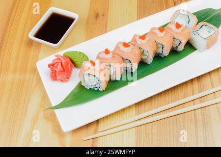 Rouleaux de sushi fraîchement préparés avec du saumon et du concombre servis sur une feuille à une table à manger Banque D'Images